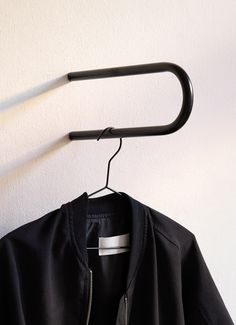 a black jacket hanging on a white wall next to a hanger with a metal bar