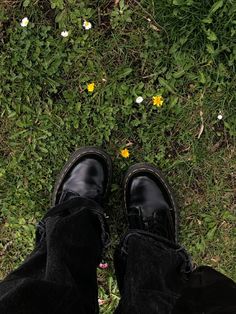 someone's feet in black shoes standing on the grass with yellow and white flowers