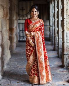 a woman in a red and gold sari standing on a stone walkway with columns