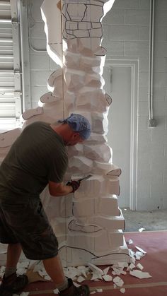 a man is working on a sculpture made out of white paper and cardboard boxes that are stacked high in the air