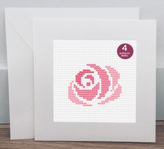 a white card with a pink cross stitch rose on it