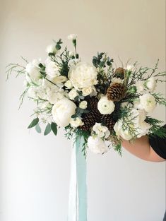 a vase filled with white flowers and pine cones