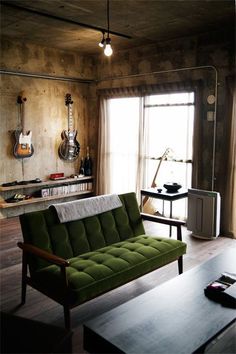 a living room with a green couch and guitar on the wall next to a window