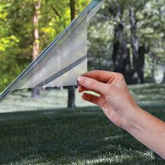 a hand is holding up a piece of paper in front of some trees and grass