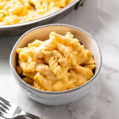 two bowls filled with macaroni and cheese on top of a white marble counter