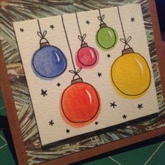 a card with three christmas ornaments hanging from it's sides, on top of a table