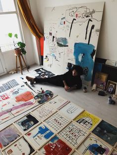 a woman is sitting on the floor in front of many drawings and paintings that are spread out