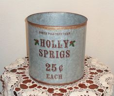 an old tin can with holly springs on it sitting on a doily next to a white wall