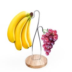 a bunch of bananas and some grapes on a wooden stand with a metal hook attached to it