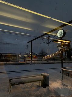 a bench sitting in front of a train station covered in snow at night with the lights on