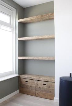 an empty room with shelves and drawers in the corner, next to a large window