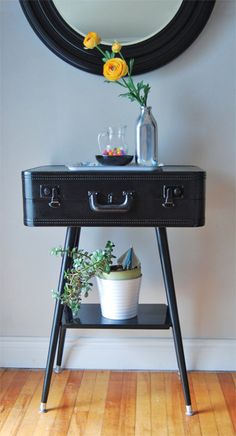 a black table with a mirror and flowers on it in front of a white wall