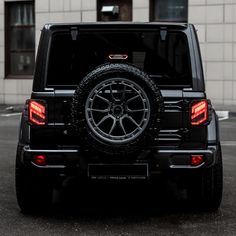 the back end of a black jeep parked in a parking lot next to a building