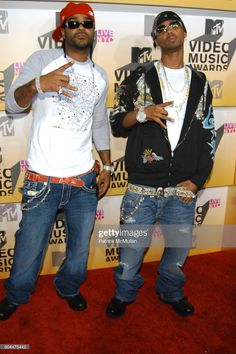 two young men standing on the red carpet at an awards event, one holding his hand up