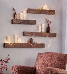 three wooden shelves with candles on them in the corner of a living room, one is decorated with christmas lights and the other has a red chair