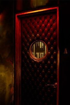 a red door with a round mirror on it's side in a dark room