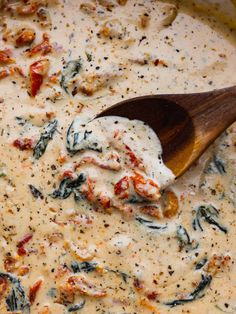 a wooden spoon in a white sauce with spinach and cheese on the top,