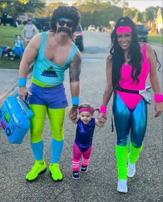 a man and woman in bodysuits walking down the street with a baby girl