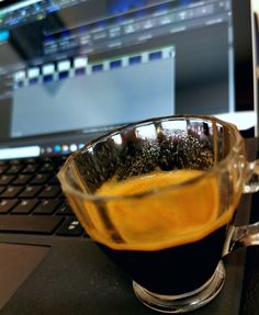 a glass cup filled with liquid sitting on top of a laptop computer