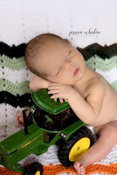 a baby laying on top of a green toy tractor