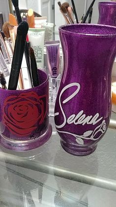 two purple vases sitting on top of a counter next to other cosmetics and makeup products