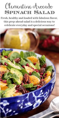 a blue bowl filled with spinach salad and topped with nuts, avocado and pomegranate