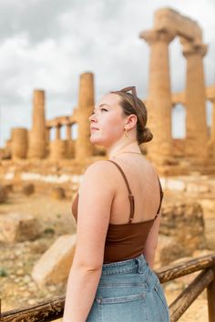 a woman standing in front of the ruins of an ancient city, looking off into the distance