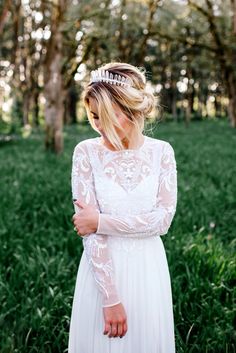 a woman wearing a white dress and a tiara standing in the grass with trees behind her