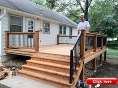 a man standing on top of a wooden deck next to a white house and trees