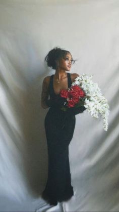 a woman in a long black dress holding white and red flowers with her right hand