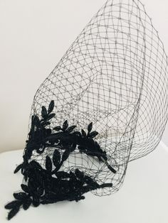 a black net hat with flowers on the front and side, sitting on a white surface