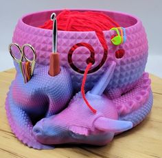 there is a pink and purple container with scissors, yarn and other items in it