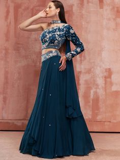 A three-piece teal blue one shoulder lehenga set from the Suruchi Parakh collection. This beautiful teal blue high-low layered flared lehenga is paired with a hand-embroidered one shoulder blouse. The teal blue color with zardozi work enhances the graceful georgette crepe and satin silk lehenga set. The lehenga has an embroidered belt to the waistline. The hand-embroidered one shoulder blouse has intricated floral embroidery with back hook opening. The outfit is completed with a teal blue choker One Shoulder Dress With Zari Work For Designer Wear, One-shoulder Georgette Wedding Set, Bollywood Style One-shoulder Fitted Pre-draped Saree, Fitted One-shoulder Pre-draped Saree For Designer Wear, One-shoulder Lehenga For Festive Reception, One-shoulder Festive Lehenga For Reception, Festive One-shoulder Lehenga For Reception, Elegant One Shoulder Choli For Festive Occasions, Bollywood One Shoulder Designer Wear Set