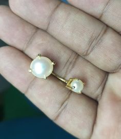 a person is holding some kind of gold and white pearl earring in their hand