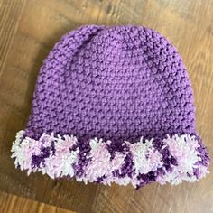 a crocheted purple hat with white and pink flowers on the side sitting on a wooden surface