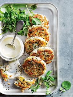 some food is sitting on a tray with sauce and greens next to it, including crab cakes