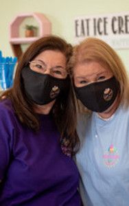 two women wearing face masks in front of a sign