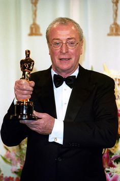 an older man in a tuxedo holding up his oscar statue