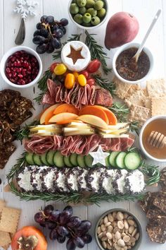 a platter filled with meats, cheeses, crackers and fruit on top of a white table