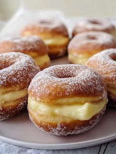 doughnuts with icing and powdered sugar are arranged on a white plate