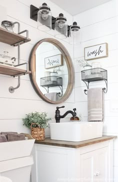 a bathroom sink under a round mirror next to a shelf with towels and baskets on it