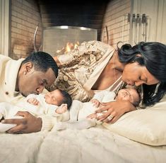 a man and woman are laying on a bed with two babies in front of a fire place