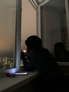 a person sitting on a window sill looking out at the city lights in the distance