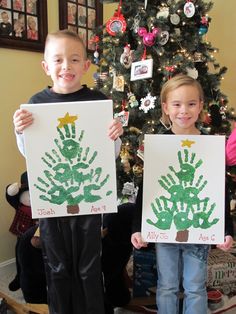 two children holding up their handprints in front of a christmas tree