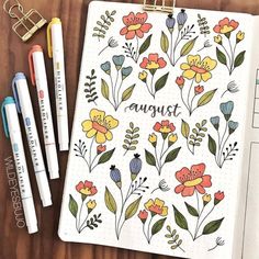 an open notebook with flowers and the words august written on it next to some markers