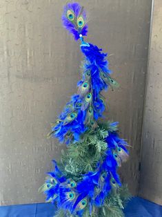 a blue and green tree with peacock feathers on it's top, in front of a wall