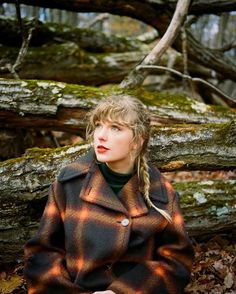 a woman with braids standing in front of some trees and mossy rocks, looking off to the side