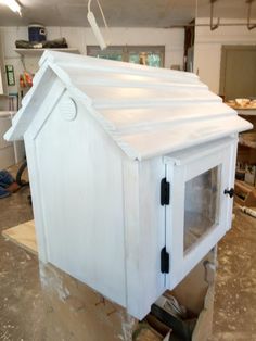 a small white house sitting on top of a piece of plywood in a garage