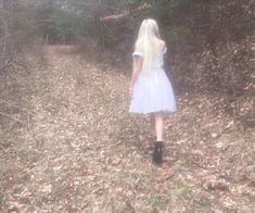 a woman in a white dress is walking through the woods with her back to the camera