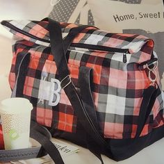 a plaid duffel bag sitting on top of a table next to a cup and other items